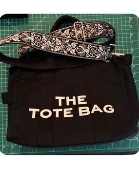 Black tote bag with white text reading 'THE TOTE BAG' and white/black